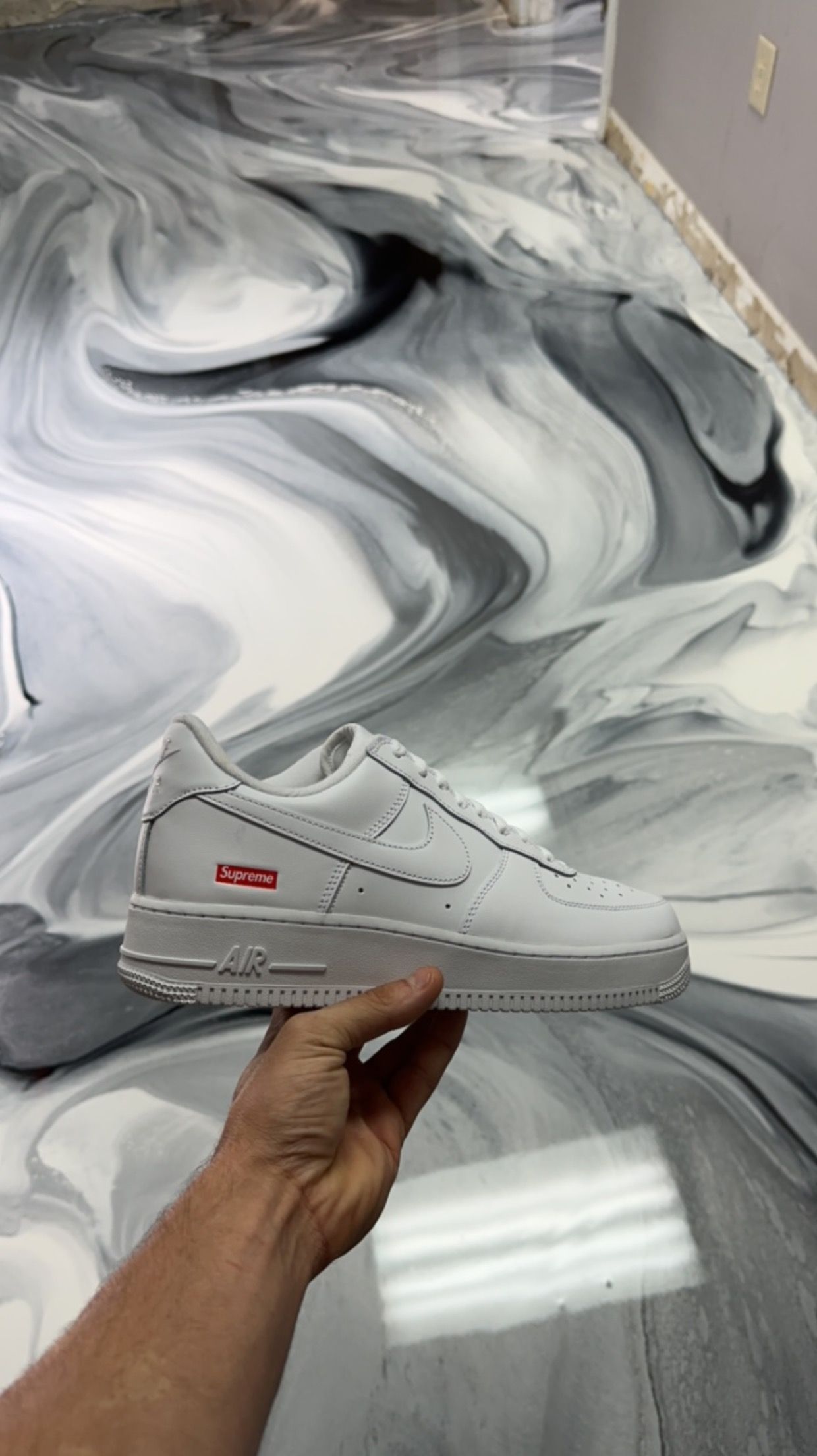 Hand holding a white sneaker against a black-and-white marbled floor background