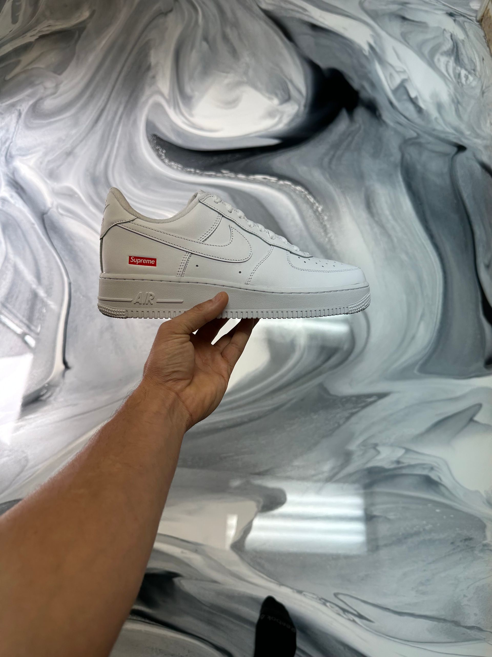 Hand holding a white sneaker against a gray marbled background