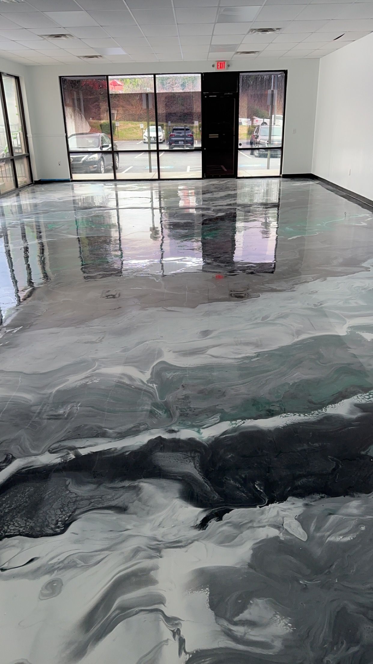 Empty office hallway with a glossy gray floor and black-and-white marbled pattern, reflecting the windows.