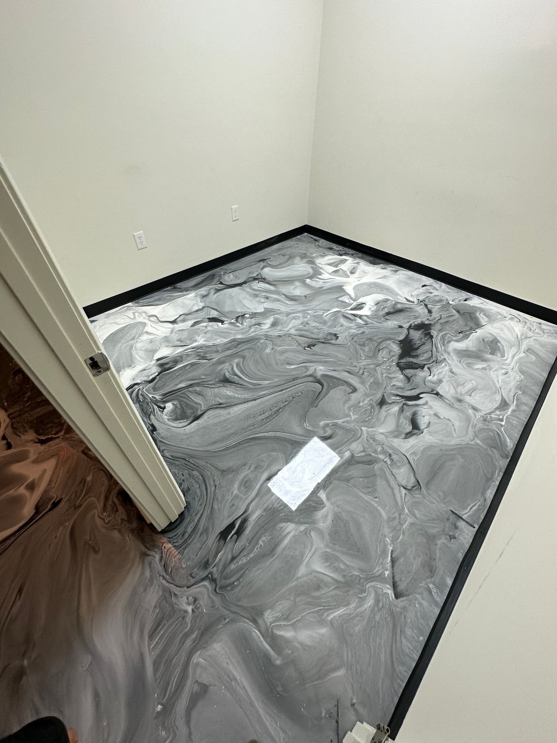 Small empty room with gray concrete floor, black baseboards, and a white door frame.