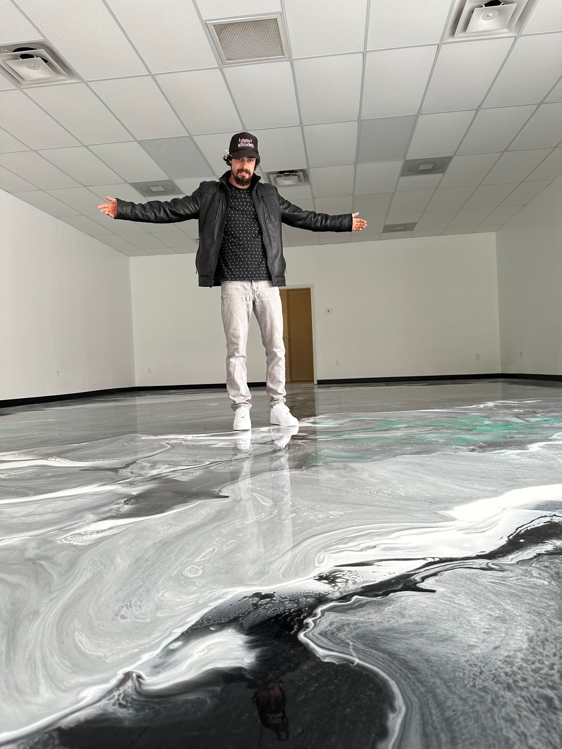 Person standing with arms outstretched in an empty room with a black-and-white abstract floor mural.