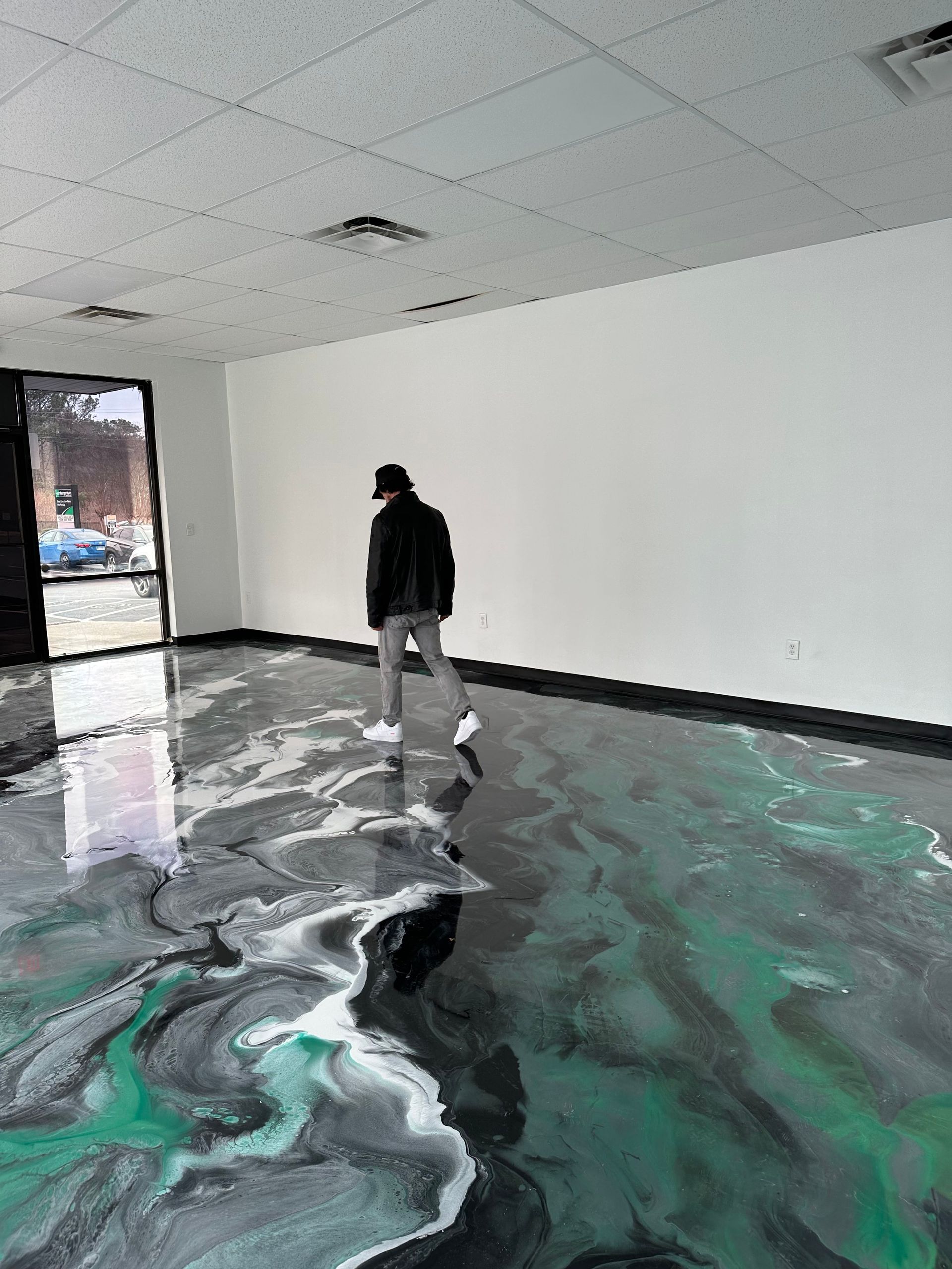 Person walking across a glossy black-and-green floor in a mostly empty white room