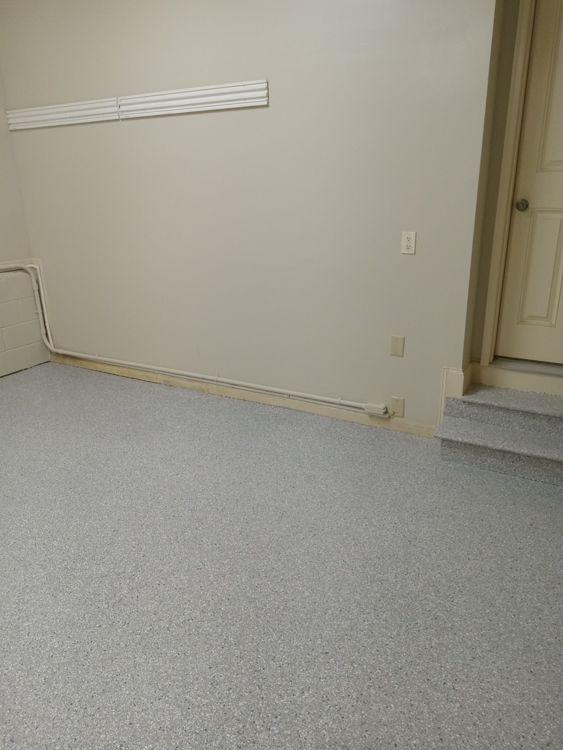 Empty beige room with carpeted floor, wall trim, electrical outlets, and a step up to a doorway.
