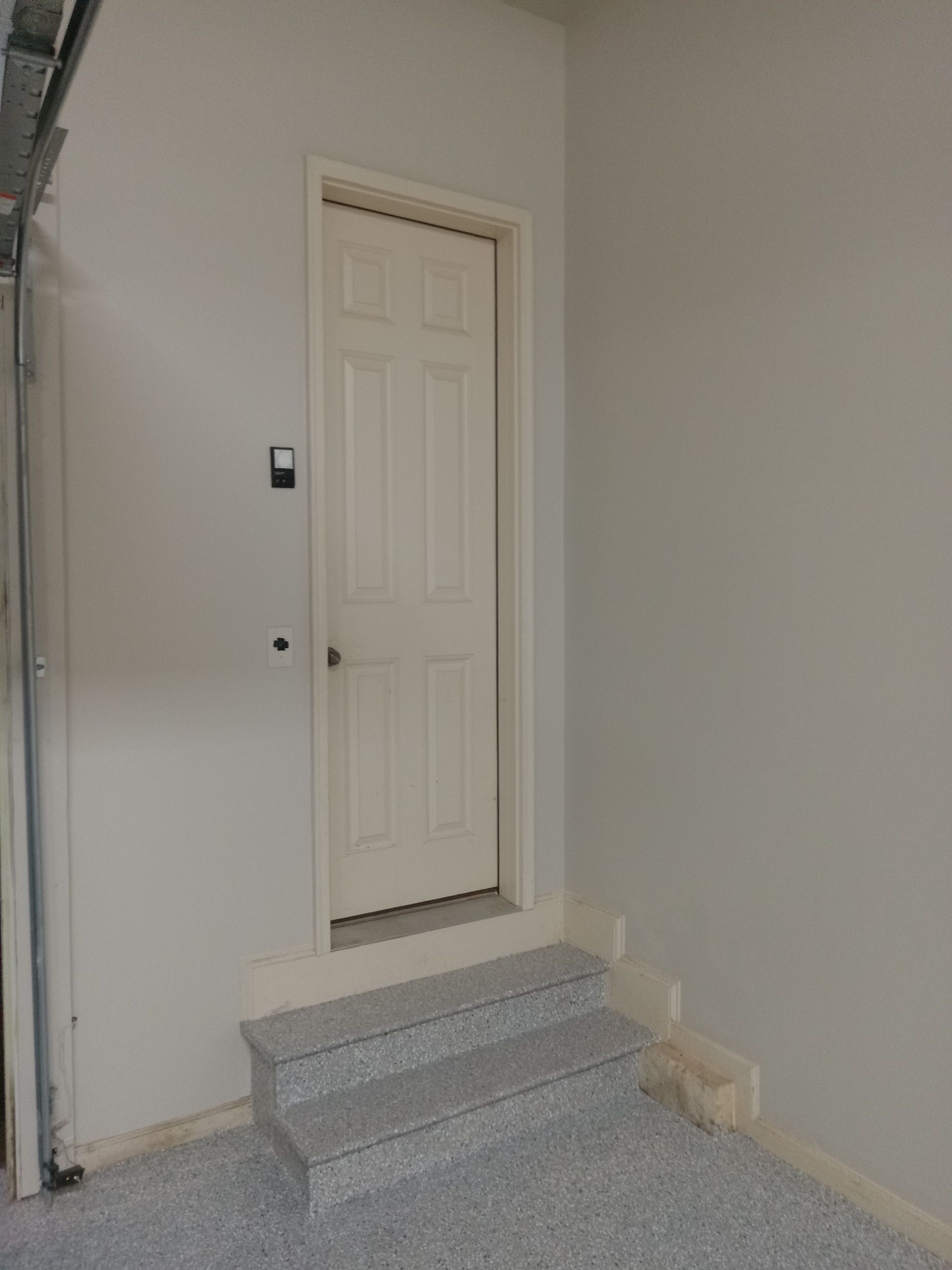 Small concrete steps leading to a white door in a plain interior wall.