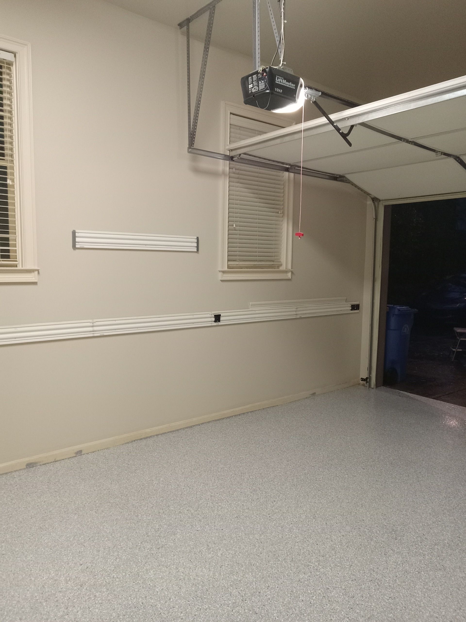 Empty garage interior with beige walls, windows, and a ceiling-mounted garage door opener.