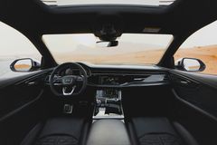 Interieurbeeld vanuit het dashboard van een auto, met uitzicht op een uitgestrekt, zanderig woestijnlandschap onder een heldere hemel.