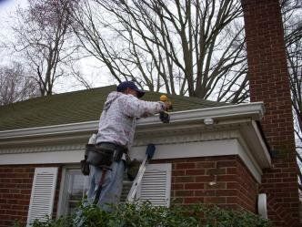A man is standing on a ladder working on the roof of a house.