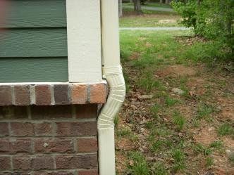 A white gutter is attached to the side of a brick house.