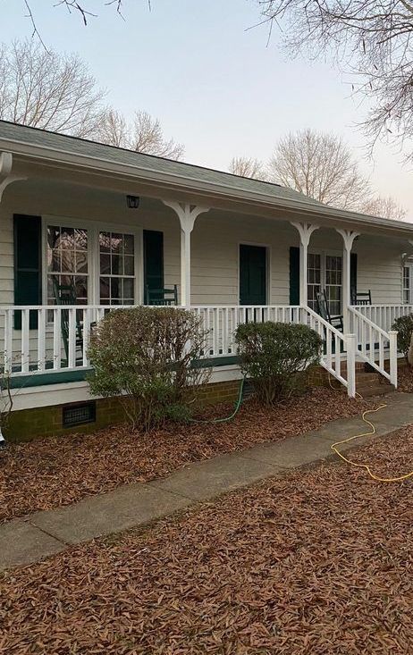 A white house with a large porch and green shutters.