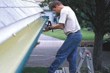 A man is standing on a ladder fixing a gutter.
