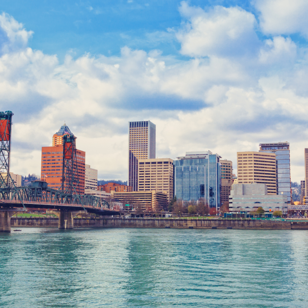 Skyline of Portland, Oregon, with river and bridge in foreground, blue sky with clouds.