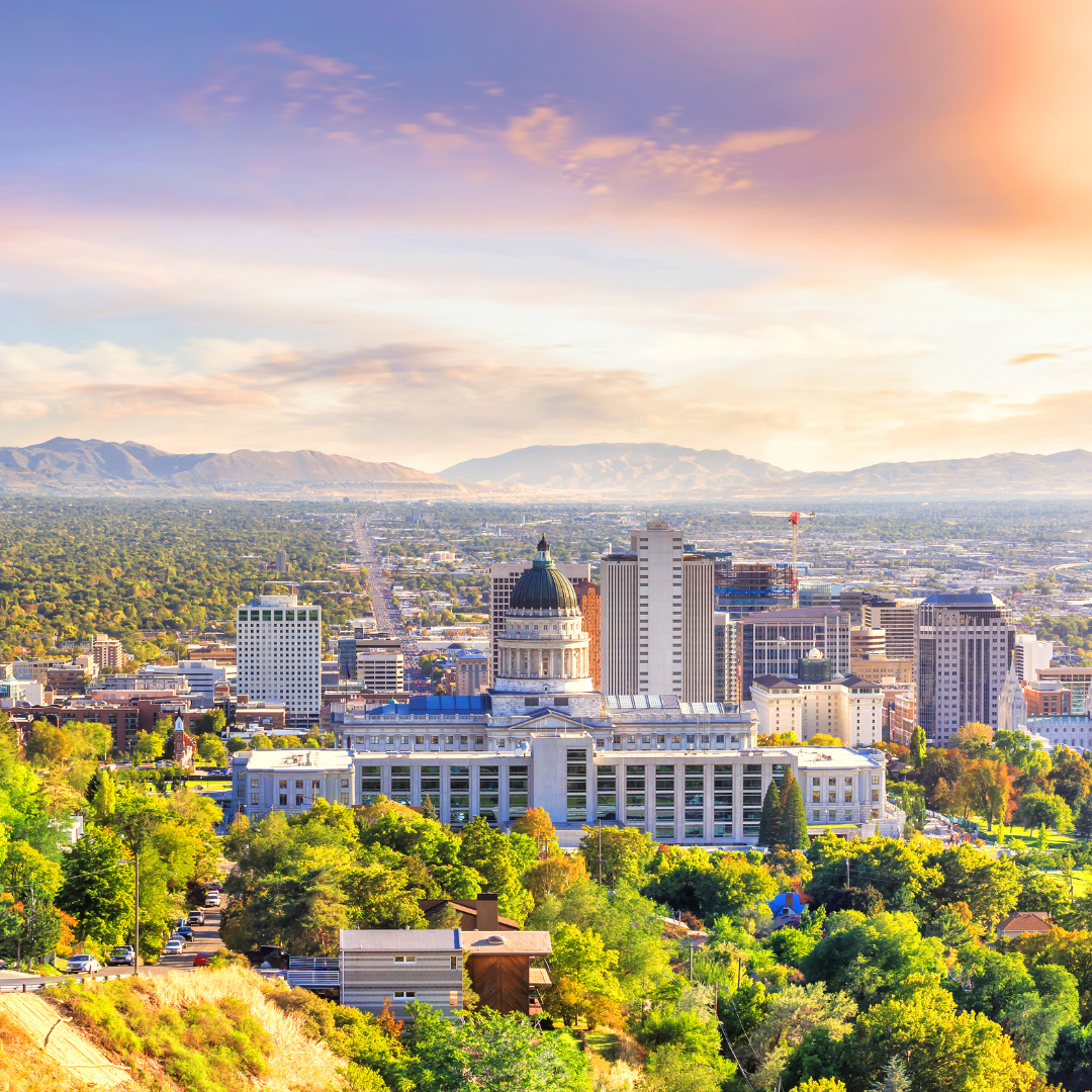 Salt Lake City skyline with mountains in the background under a colorful sunset.