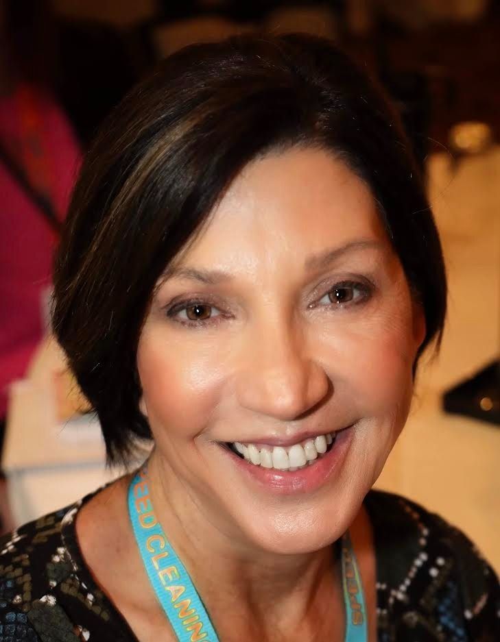 Smiling woman with dark hair wearing a turquoise lanyard in a warmly lit indoor setting