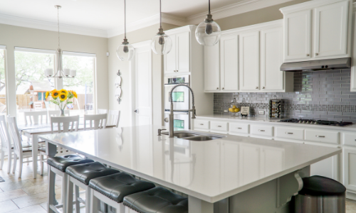 Bright modern white kitchen with a large island, barstools, and dining area by sunlit windows