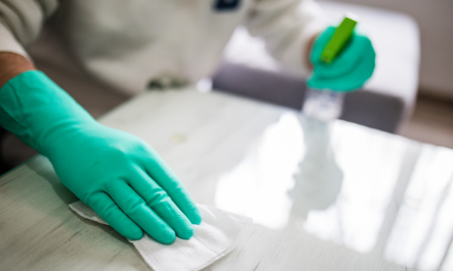 Person in green gloves wiping a shiny white surface with a cloth and spray bottle