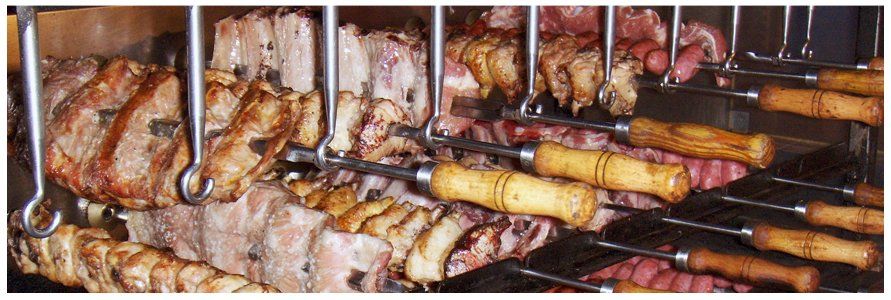 Um monte de carne está sendo cozido em espetos em uma grelha