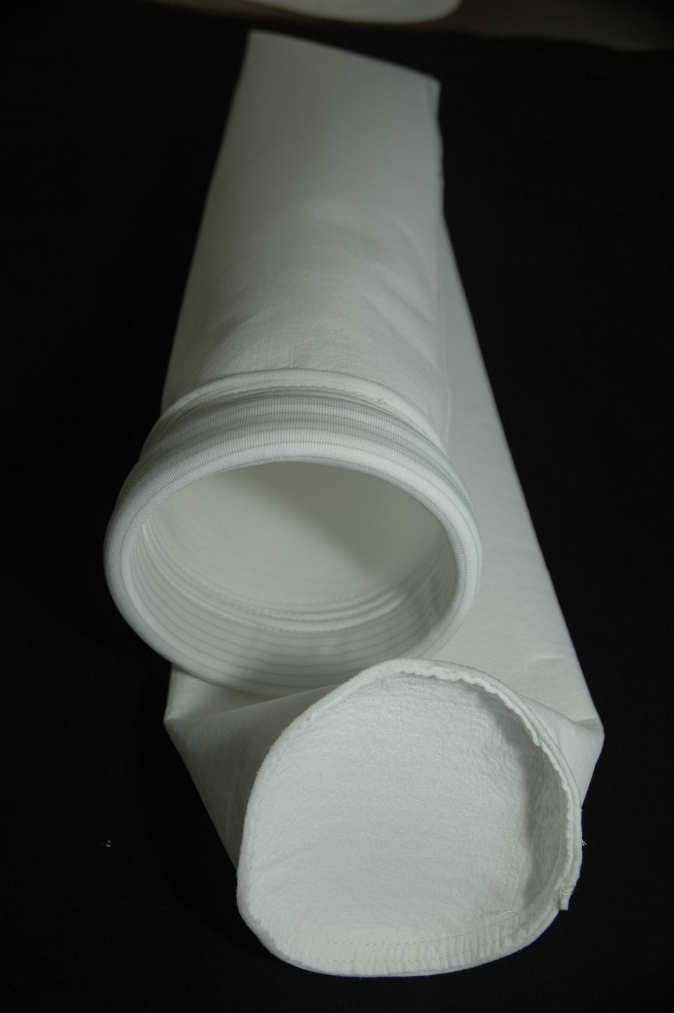 Sac filtrant industriel cylindrique blanc, ouvert aux deux extrémités, sur fond noir.