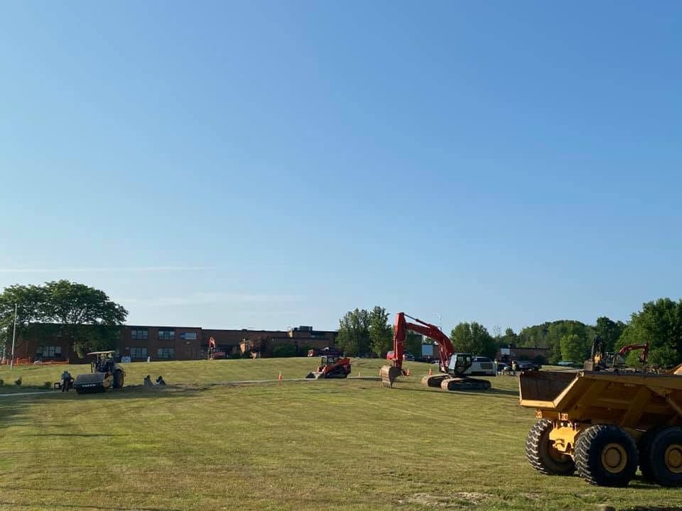 Construction equipment on a grassy field at a worksite under a clear blue sky.