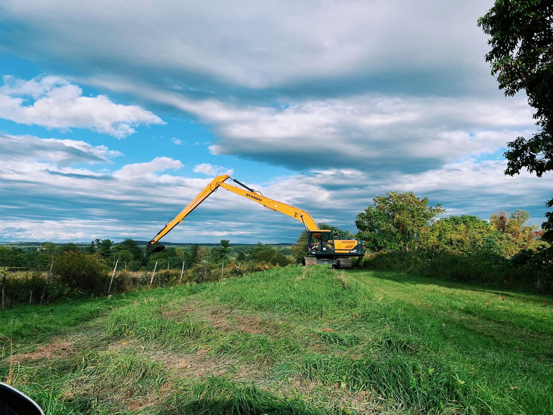 Yellow excavator working in a green field under a cloudy blue sky