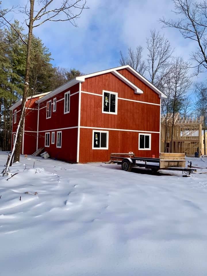Red two-story house with white trim in a snowy yard, trees and blue sky in the background