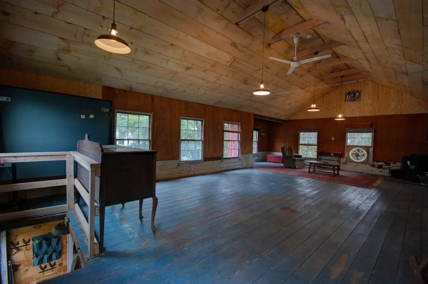 Spacious rustic loft with wood-paneled walls, arched ceiling, hanging lights, and a large open floor.