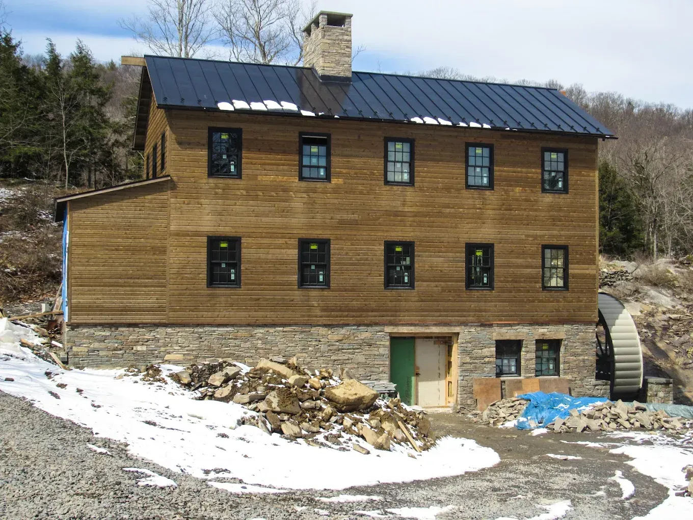 Wooden house on a snowy hillside with a black roof and stone chimney