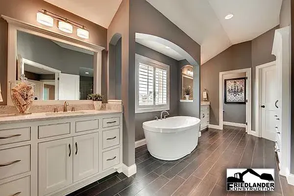 Bright modern bathroom with freestanding tub, double vanity, gray walls, and dark wood floor