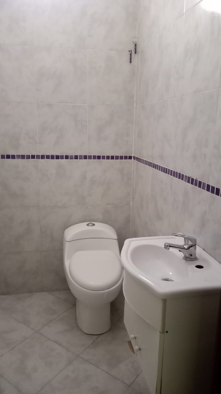 Un baño pequeño con inodoro y lavabo blancos con grifería cromada. Las paredes y el suelo están alicatados en gris y blanco.