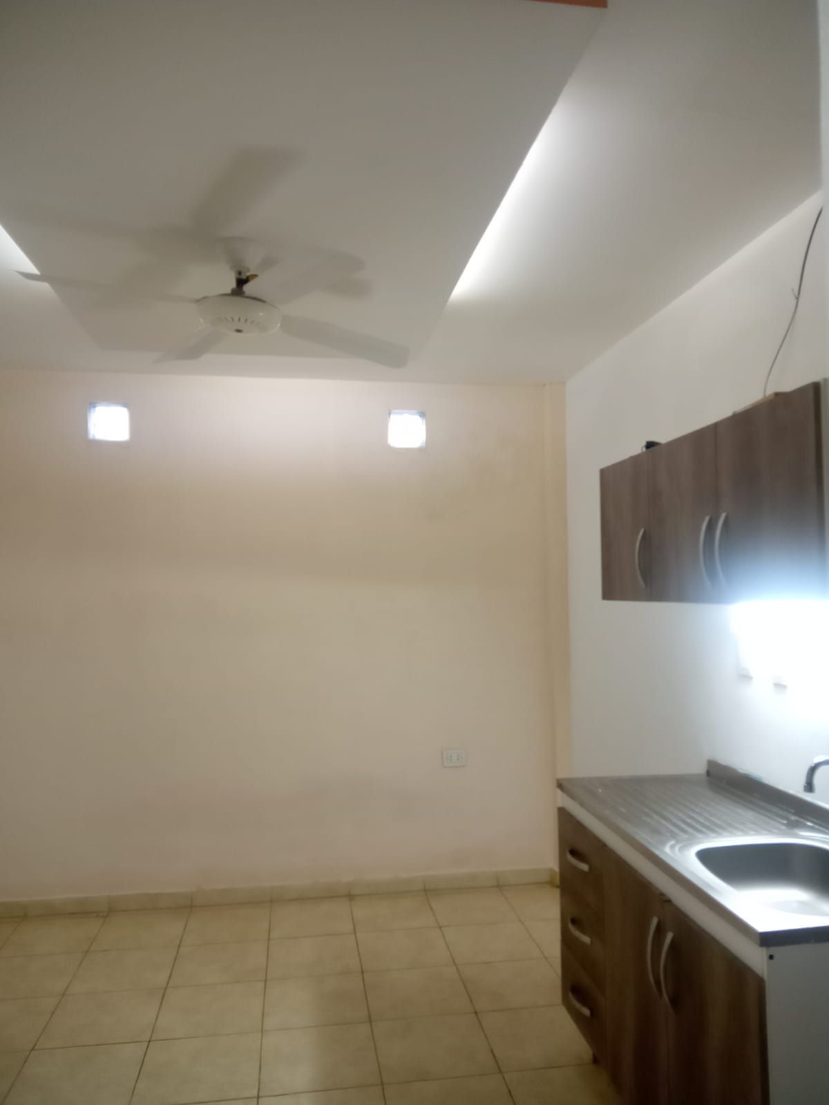 Cocina vacía con ventilador de techo y armarios. Las paredes son beige y el suelo es de baldosas.