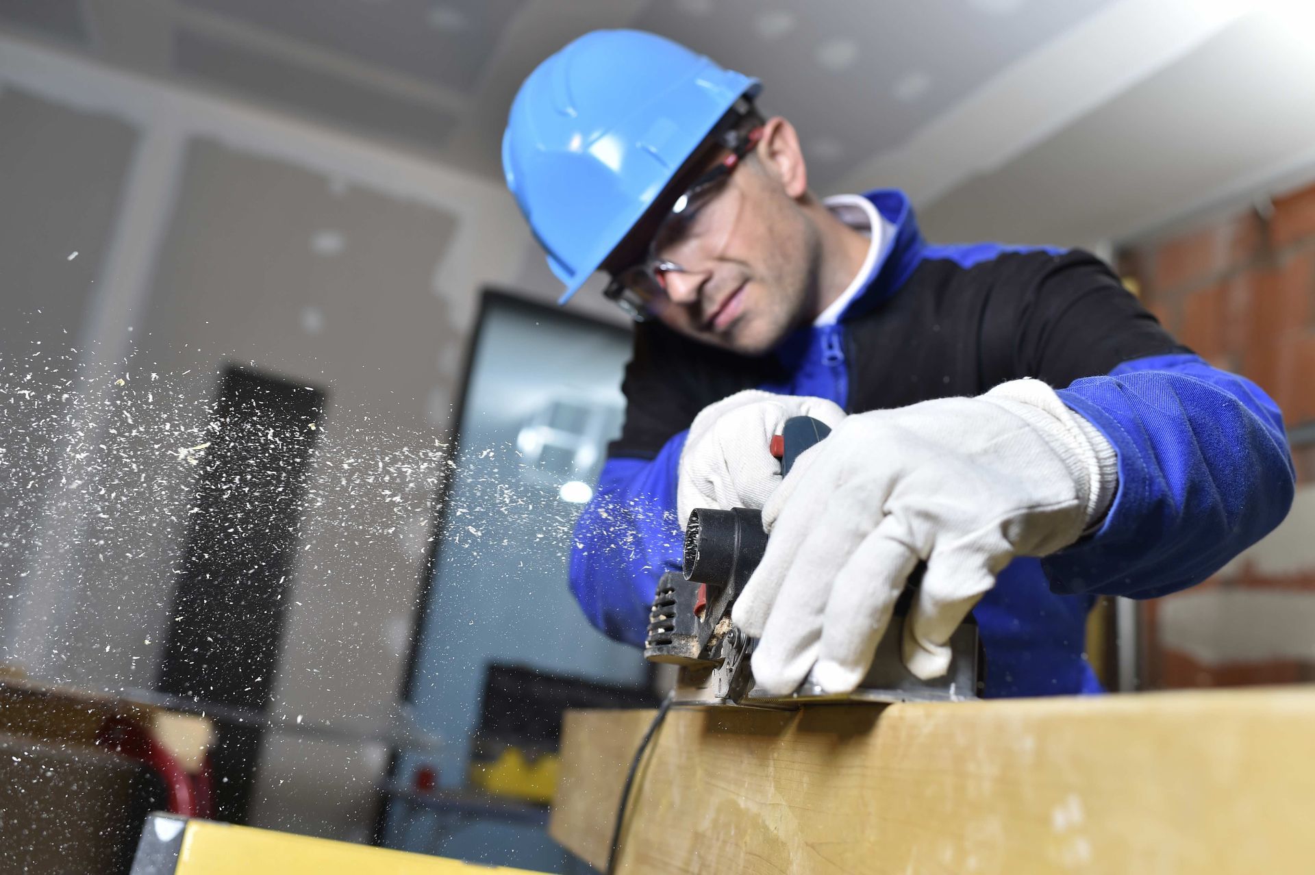 a man wearing a hard hat and safety glasses is cutting a piece of wood