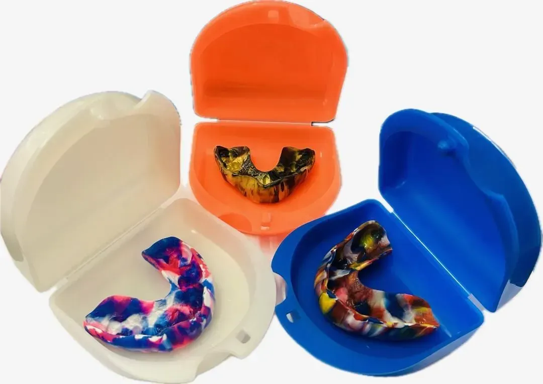 Three Open Cases in Cream, Orange, and Blue, Each Holding a Colorful Mouthguard — Precise Dentures in Berserker, QLD