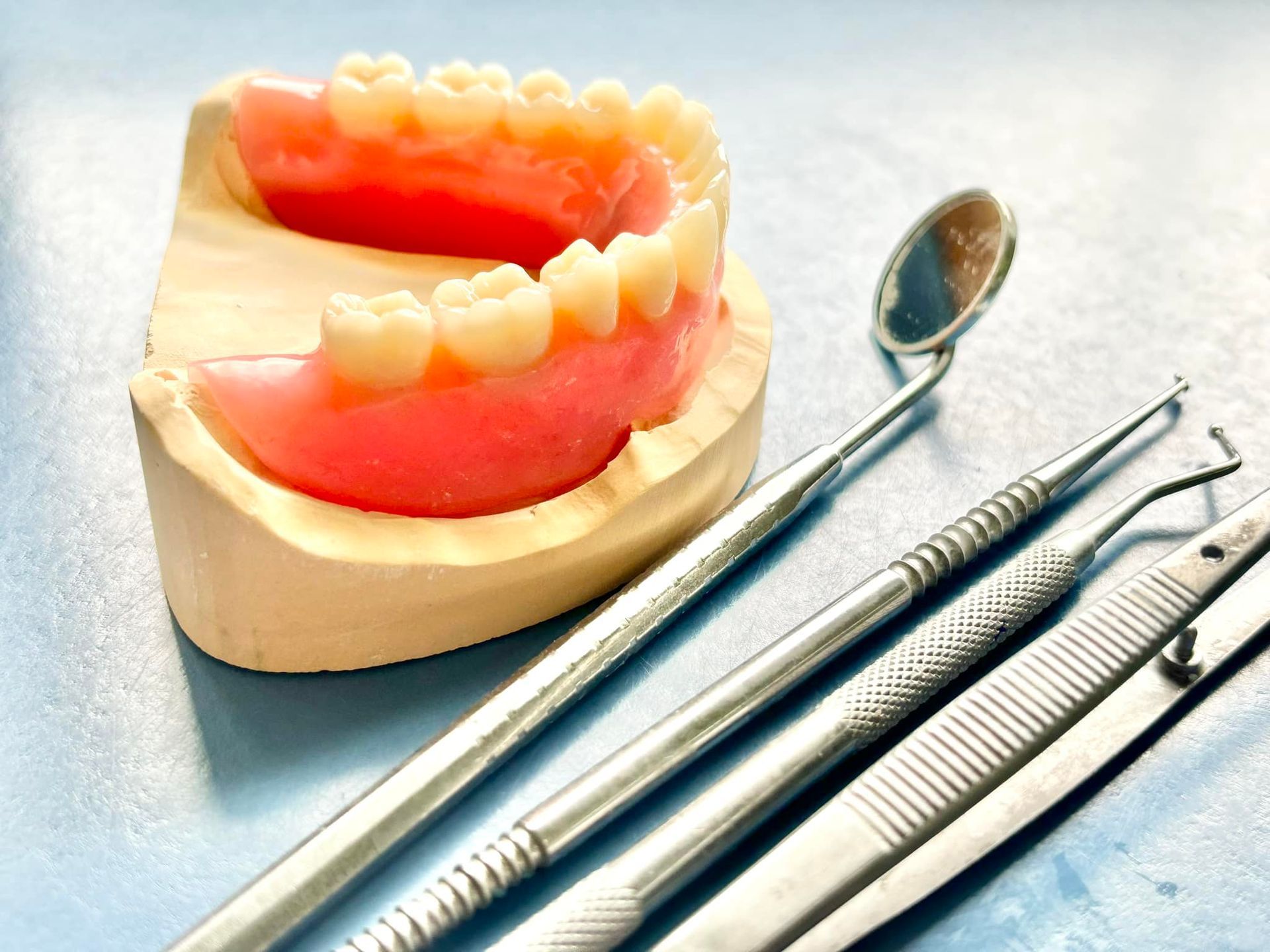 Dentures with dental tools on a light blue surface — Precise Dentures in Berserker, QLD