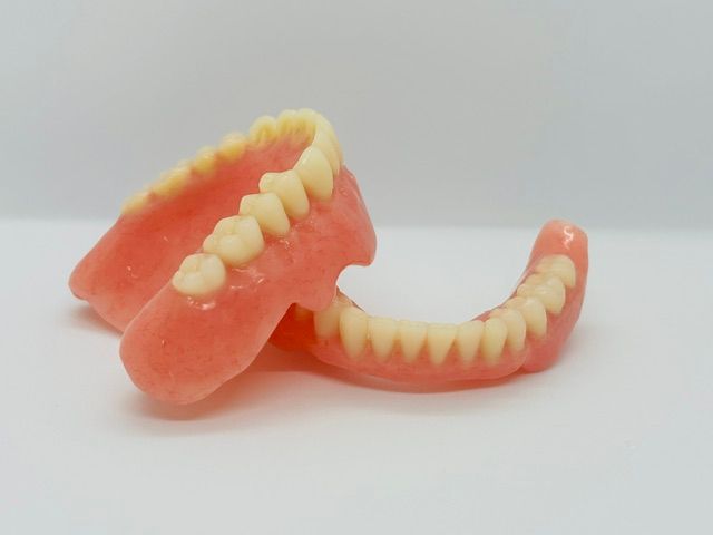 Two plastic dentures with pink gums and white teeth on a light background — Precise Dentures in Berserker, QLD