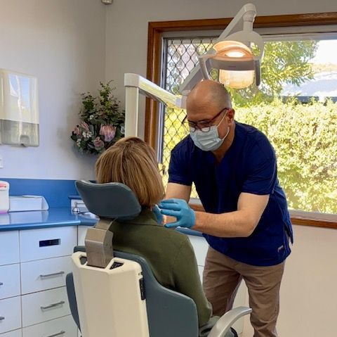 Dentist examining a patient in a bright clinic room under an overhead dental light  — Precise Dentures in Berserker, QLD