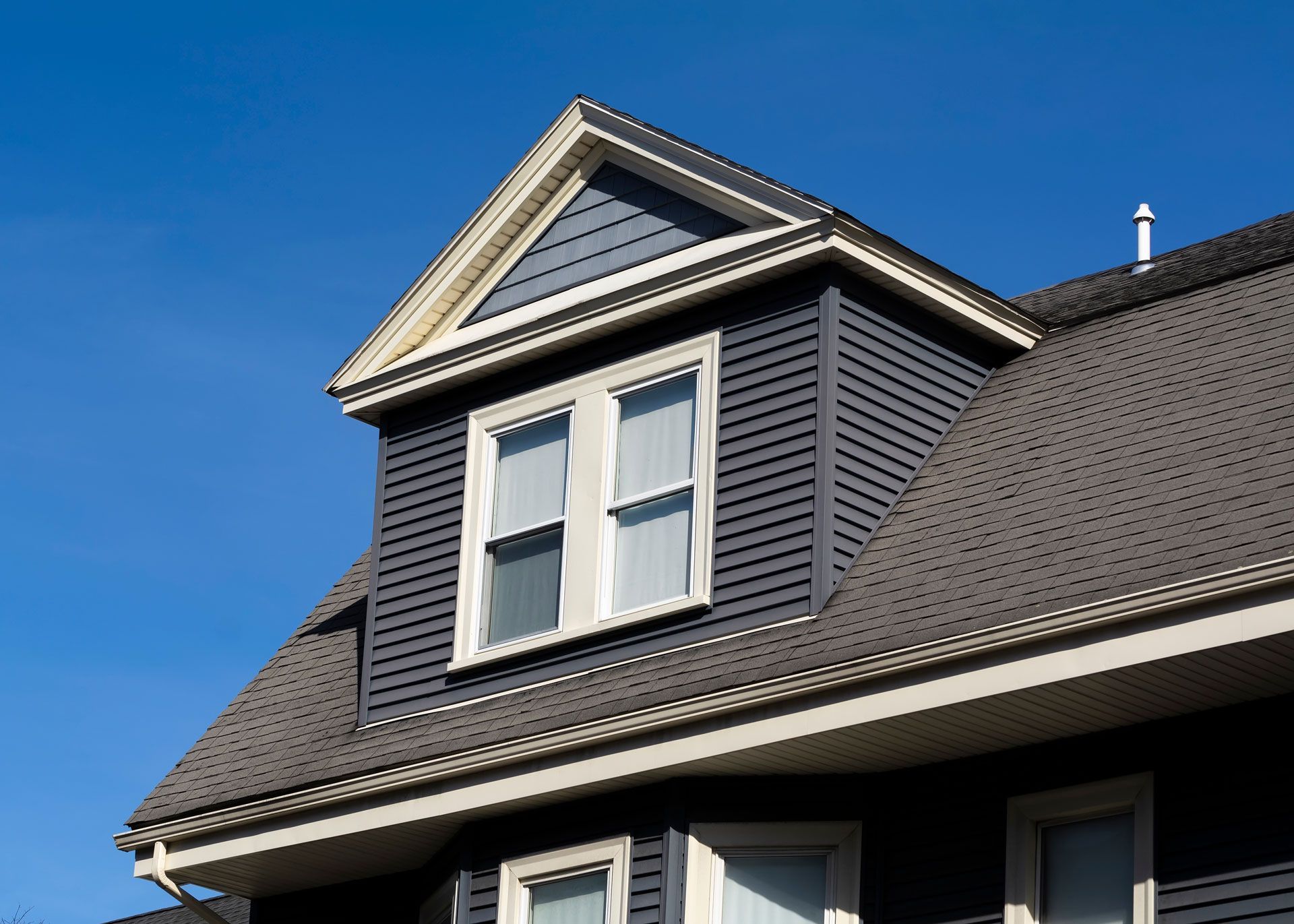 Blue house with gray roof, dormer window, and blue siding against a clear sky.