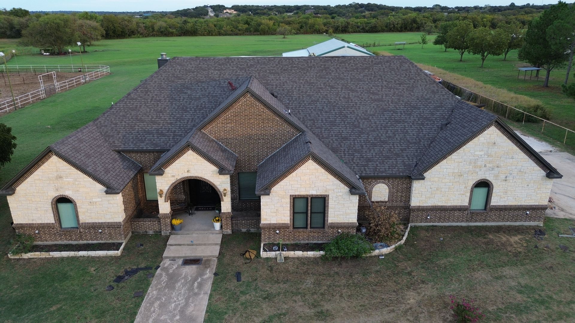 Large stone house with dark roof, arched entryway, and front walkway in a green rural setting
