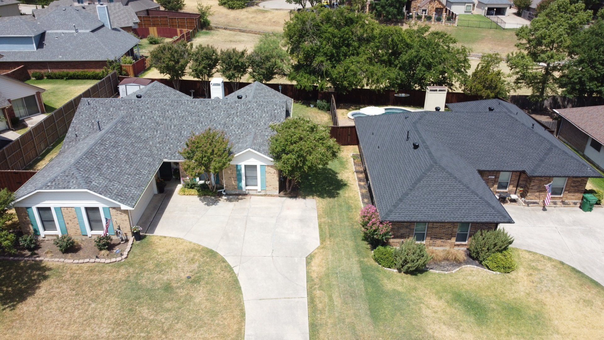 Aerial view of two suburban houses with driveways, lawns, and trees on a sunny day