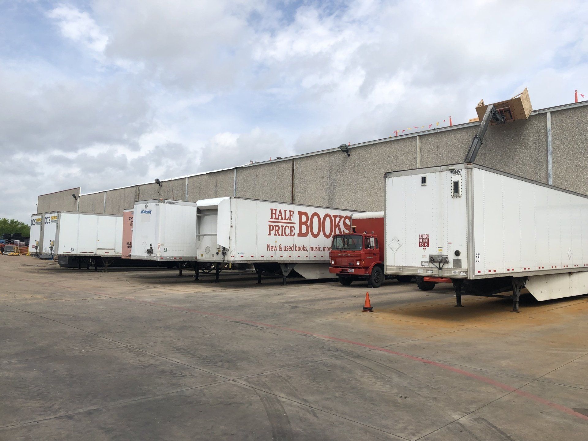 White semi-trailers parked beside a warehouse under a cloudy sky
