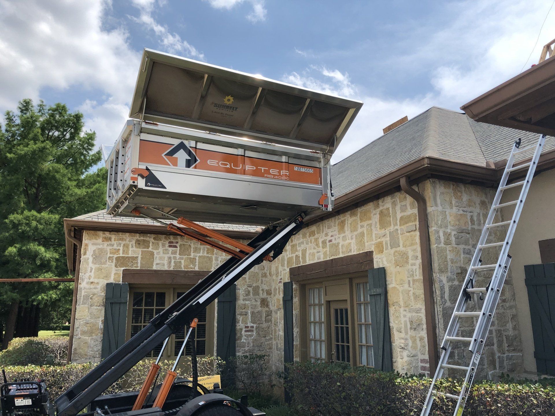 Stone house with roof repair lift and ladder under a partly open roof, outdoors in daylight