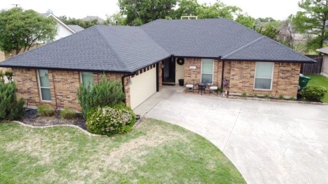 Single-story brick house with dark roof, front driveway, and green lawn.