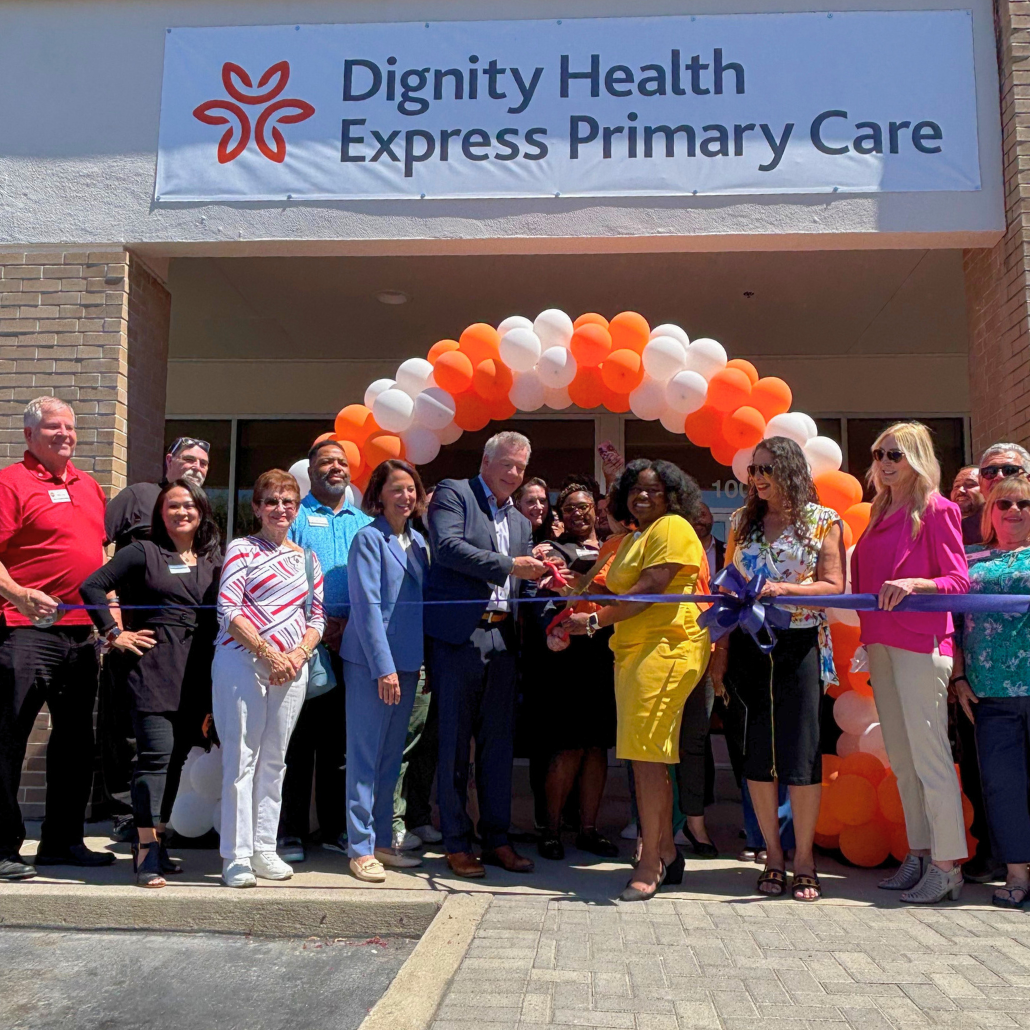 People cutting ribbon at Dignity Health Express Primary Care opening with orange and white balloon arch.