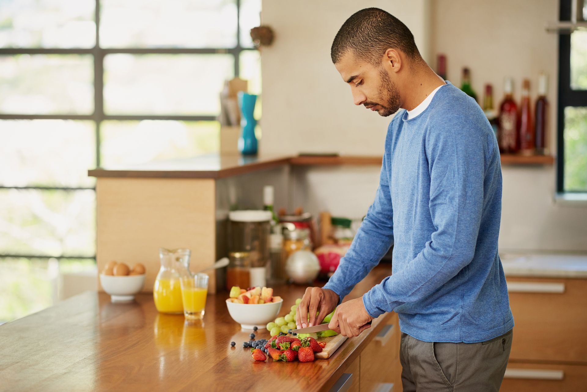 A man is cutting fruit on a cutting board in a kitchen.