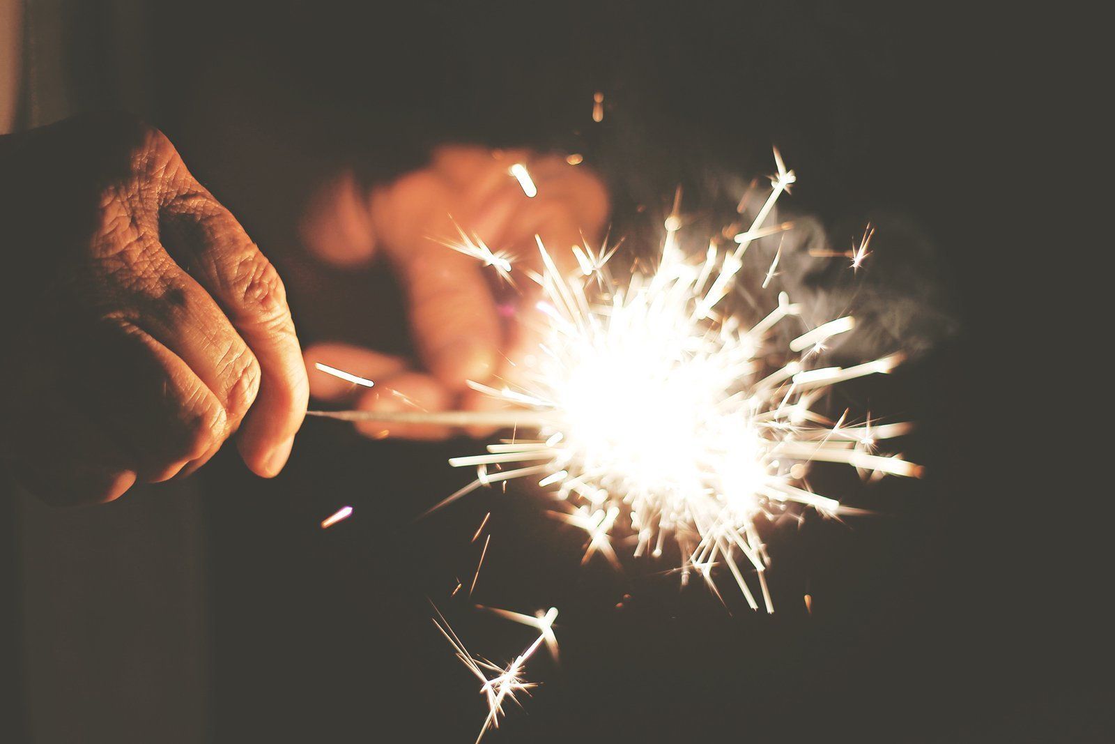 A person is holding a sparkler in their hand in the dark.