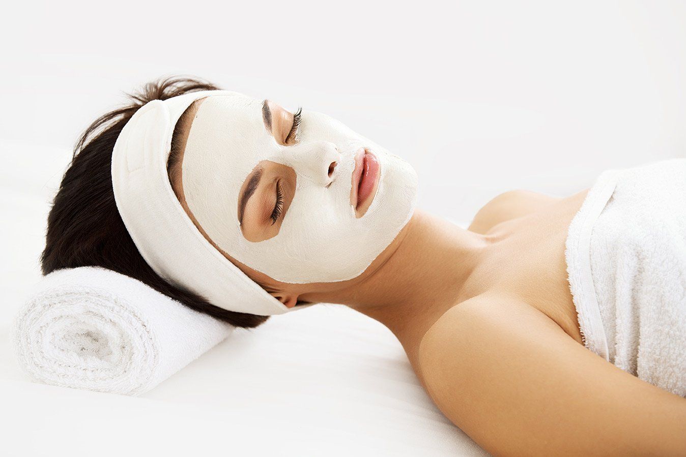 A woman is laying on a bed with a white mask on her face.