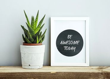 A potted plant is sitting on a wooden shelf next to a framed picture that says `` be awesome today ''.