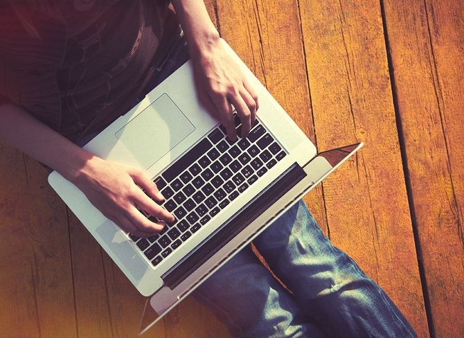 shawn torres from regency home loans is typing on a laptop computer while sitting on a wooden floor.