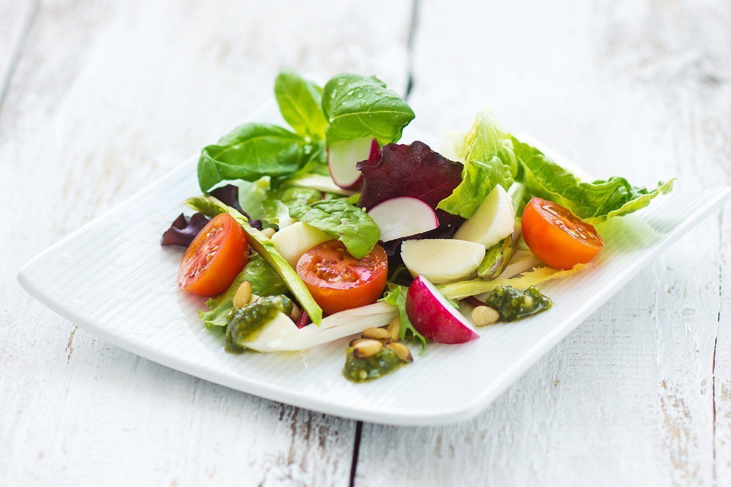 Salad with tomatoes, mozzarella, radish, and basil on a white plate.