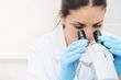 Scientist using a microscope while wearing blue gloves in a lab