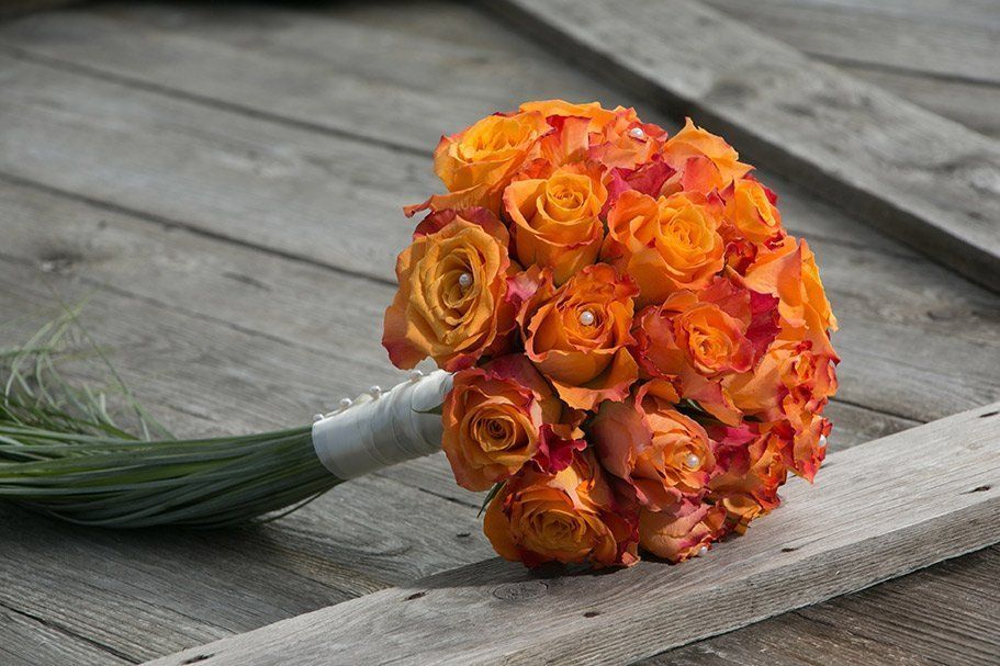 A bouquet of orange roses is sitting on a wooden table.