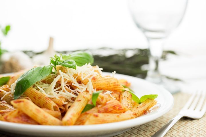 Plate of penne pasta with tomato sauce, basil, and cheese; wine glass and fork.